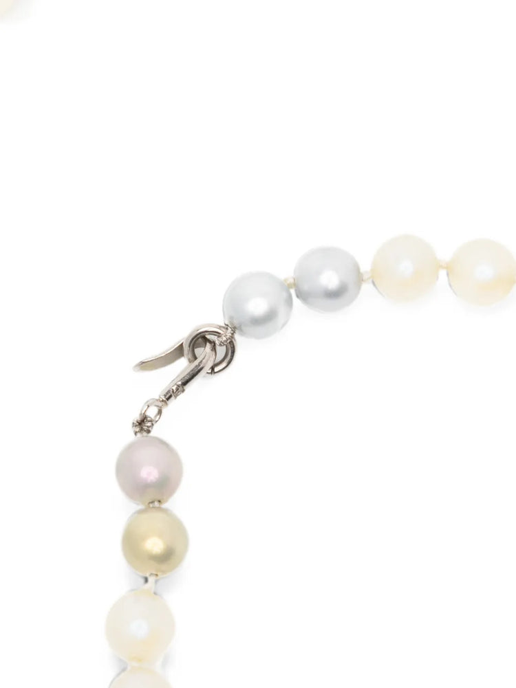 A close-up of a Chanel pearl strand necklace with mixed white, cream, and pale pink pearls, featuring a silver lobster clasp on a white background.