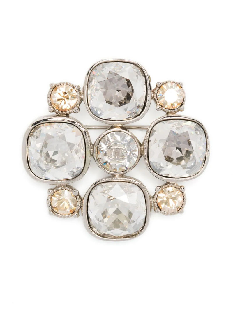 Chanel CC crystal-embellished brooch featuring sparkling rhinestones and elegant design, displayed on a neutral background.