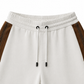 Brunello Cucinelli ivory jogger pants with elasticated drawstring waistband, brown side stripe panels, metallic trim detail, tapered leg, rolled cuffs, and relaxed tailored fit.