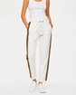 Brunello Cucinelli ivory jogger pants with elasticated drawstring waistband, brown side stripe panels, metallic trim detail, tapered leg, rolled cuffs, and relaxed tailored fit.