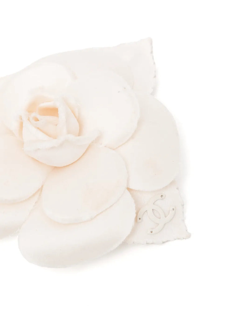 Chanel off-white fabric camellia flower brooch pin featuring layered petals and a leaf accent with a subtle cream CC logo.