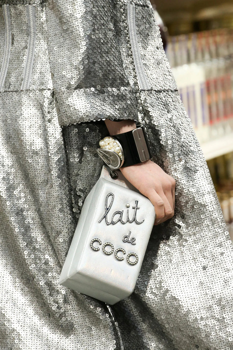 Chanel Lait de Coco Milk Carton Bag in metallic silver with structured carton shape, top handle, chain strap, pearl-style lettering and novelty runway design.