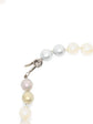 A close-up of a Chanel pearl strand necklace with mixed white, cream, and pale pink pearls, featuring a silver lobster clasp on a white background.