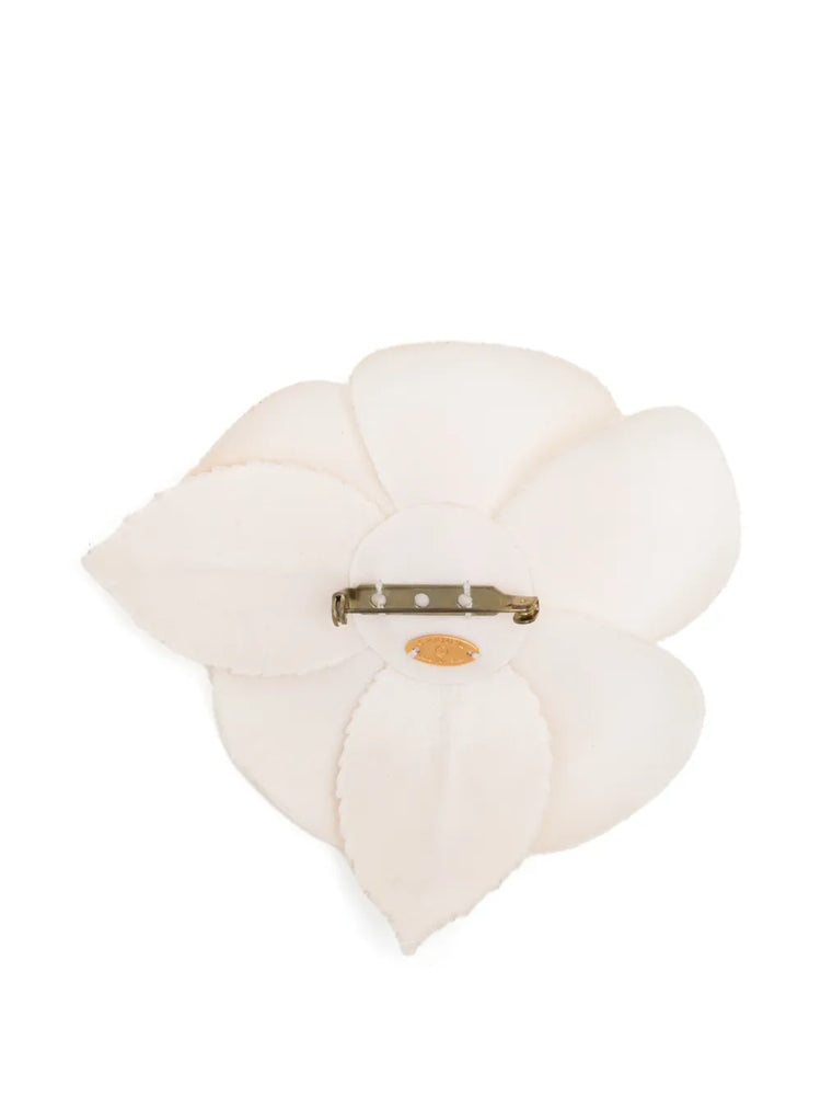 Chanel off-white fabric camellia flower brooch pin featuring layered petals and a leaf accent with a subtle cream CC logo.