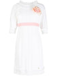 Chanel white babydoll dress with pale pink waistband, camellia flower embellishment, high ruffled neckline, short sleeves and pleated trim detailing.