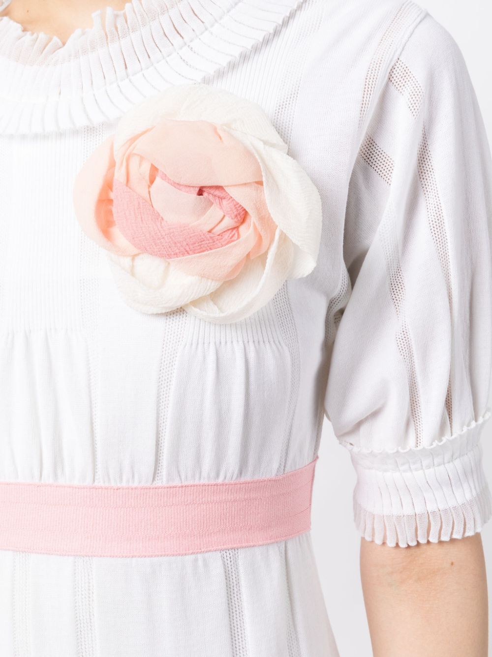 Chanel white babydoll dress with pale pink waistband, camellia flower embellishment, high ruffled neckline, short sleeves and pleated trim detailing.