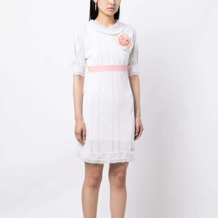 Chanel white babydoll dress with pale pink waistband, camellia flower embellishment, high ruffled neckline, short sleeves and pleated trim detailing.