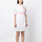 Chanel white babydoll dress with pale pink waistband, camellia flower embellishment, high ruffled neckline, short sleeves and pleated trim detailing.