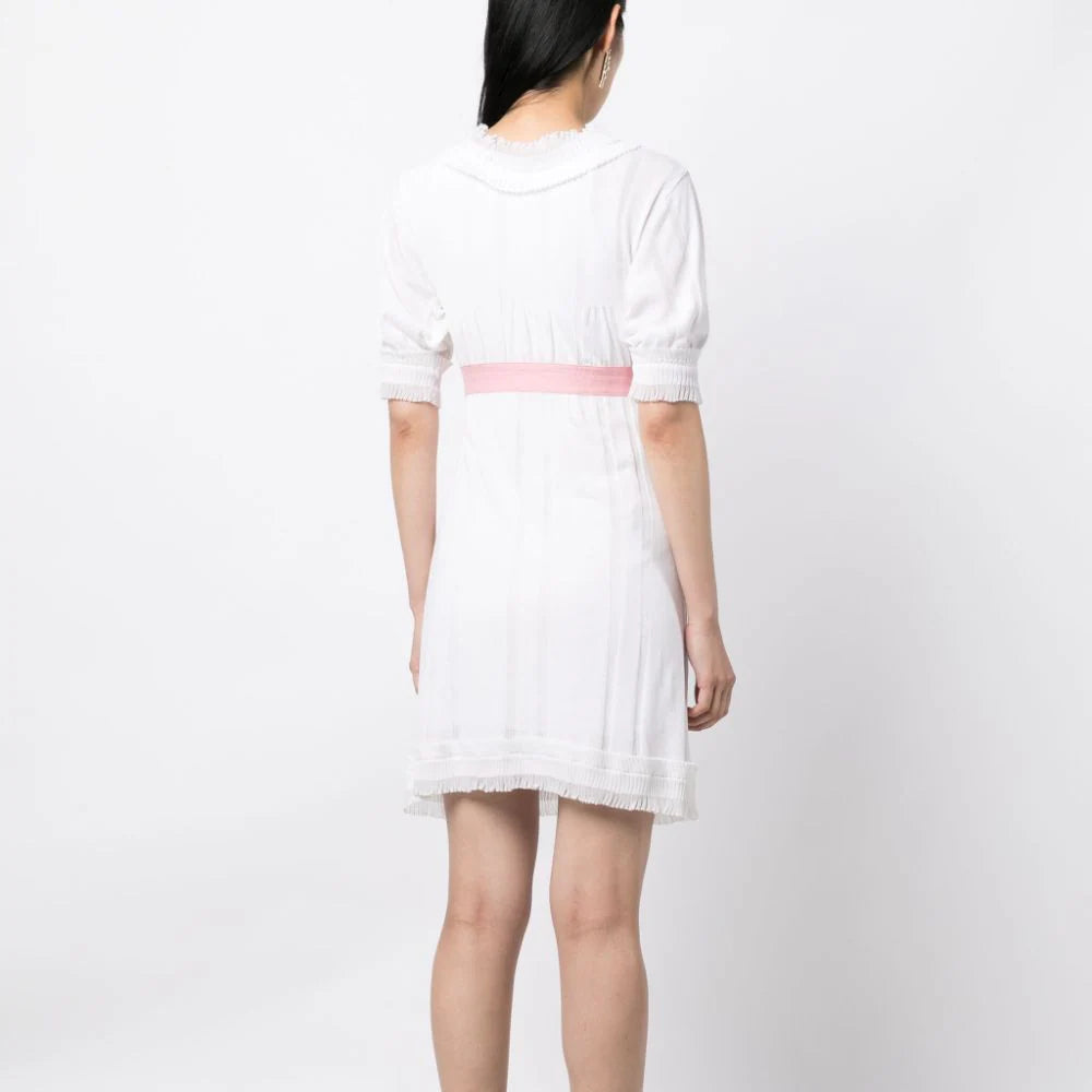 Chanel white babydoll dress with pale pink waistband, camellia flower embellishment, high ruffled neckline, short sleeves and pleated trim detailing.