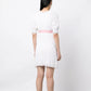 Chanel white babydoll dress with pale pink waistband, camellia flower embellishment, high ruffled neckline, short sleeves and pleated trim detailing.