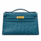 Hermès Kelly Pochette in Bleu Colvert ostrich leather with gold hardware, showcasing elegant handbag design and craftsmanship.