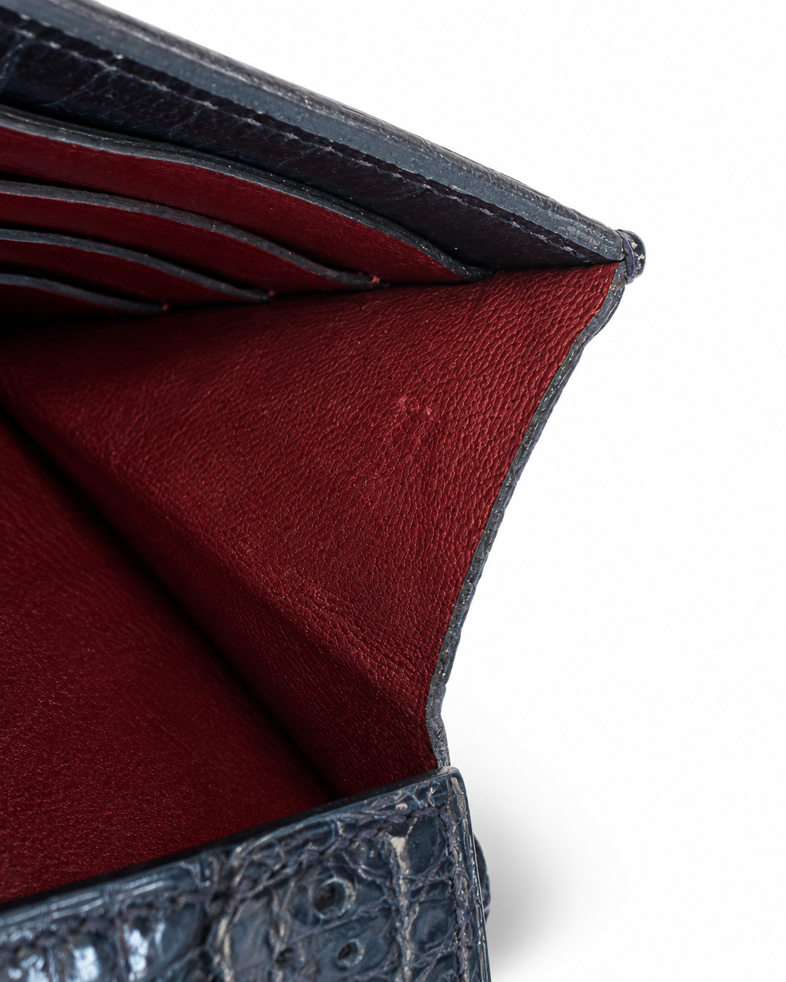 Close-up detail of a dark textured leather wallet or card holder showing the deep burgundy red interior lining and card slots on a white background.