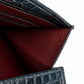 Close-up of an open leather wallet or card holder showing a deep burgundy interior and dark blue-green crocodile-embossed exterior, with a small embossed brand mark visible on the inner flap.