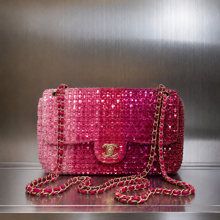 A pink Chanel shoulder bag covered in sequins, featuring a gold-tone interlocking CC turn-lock and a chain strap, set against a brushed metal background.