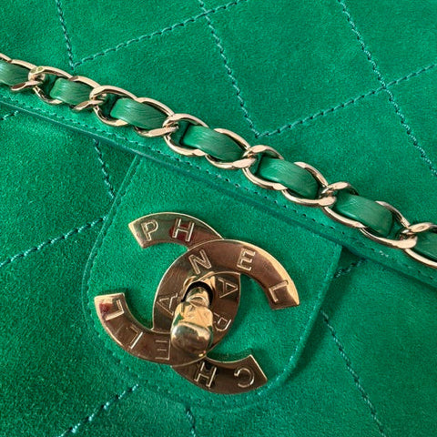 Close-up of a green quilted suede Chanel Flap Airline Pharell handbag with a gold-tone chain strap and a prominent interlocking CC logo clasp on the front flap.