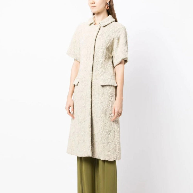 Bottega Veneta light beige short-sleeved jacquard coat with textured woven pattern, rounded collar, concealed fastening and flap pockets.