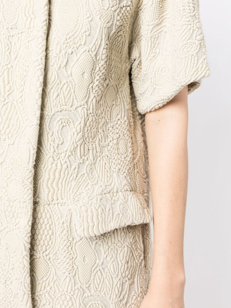 Bottega Veneta light beige short-sleeved jacquard coat with textured woven pattern, rounded collar, concealed fastening and flap pockets.